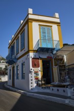Corner building in white and yellow with blue shutters, souvenir shop on a sunny street, Agia
