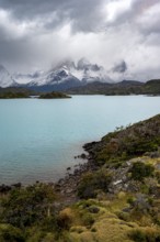 Cloudy mountain range Cuernos del Paine, shore of the blue lake Lago Pehoe in the evening light,