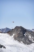 Helicopter with a load on a rope flies over glaciers and mountains, Stubai Alps, South Tyrol, Italy