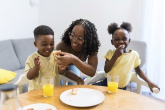 Mother joyfully feeding her children during a cozy breakfast at home, creating a warm atmosphere