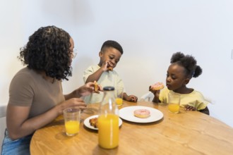 Mother and children enjoying breakfast together at home, sharing delicious donuts and refreshing
