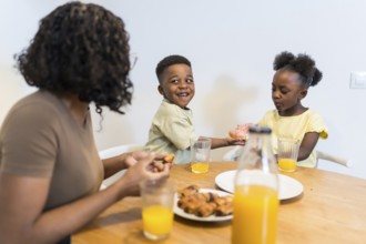 Mother and children enjoying breakfast together at the dining table, sharing donuts and orange