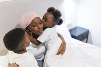Two children hugging and kissing their sick mother in bed, showing support and love during cancer
