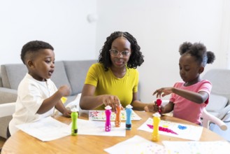 Mother and her two children enjoying creative time, painting colorful dots on paper at the dining