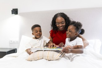 Smiling mother sharing a bedtime story with her two joyful children while cozily nestled on the