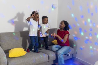 Mother and her two children enjoying dancing together in the living room, illuminated by colorful