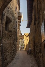 Alley in San Gimignano with historic walls, laundry in the wind and an elderly man on a chair, San