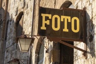 PHOTO sign in gold lettering hangs on a rustic stone wall in San Gimignano, Tuscany, Italy