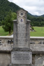 Gravestone with inscription and oval photo portrait in front of forest, Zgornje Jezersko,