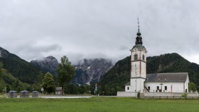 Church tower with red details in front of a mountainous landscape, Zgornje Jezersko, Gorenjska,