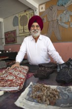 Indian Sikh, 68 years old, in his shop, in front bales of cloth and wooden panels for wood panel
