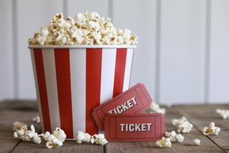 Red and white striped popcorn bucket with antique red movie tickets on rustic wooden table.