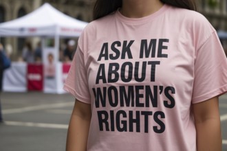 Close-up of woman in pink shirt with feminist message As me about women's rights at street info