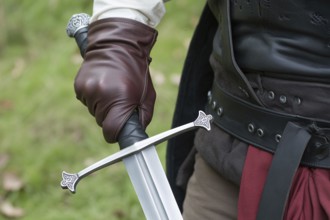 Close up of hand in leather glove holding medieval sword hilt with gemstone. Concept of medieval or