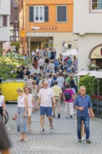People stroll through a lively old town street, surrounded by shops and summery impressions, 950