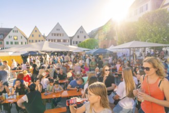 Visitors relax at tables in sunny weather, surrounded by historic house facades, 950 years Weil der