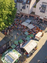 Aerial view of a town festival with numerous people and tents on a town square in sunny weather,