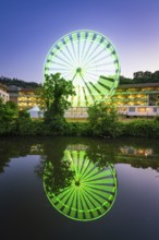 Green-blue illuminated Ferris wheel at night, reflected in the water, Calw, Germany