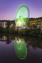 Green illuminated Ferris wheel at night, reflected in the water, Calw, Germany
