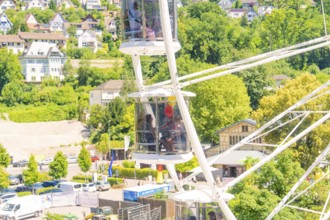 Detail of a Ferris wheel with passengers, surrounded by green trees and urban surroundings, Calw,