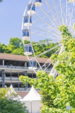 Close-up of the Ferris wheel, surrounded by green trees and tents against a blue sky, Calw, Germany
