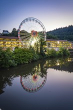 Illuminated Ferris wheel in a wooded landscape reflected in the water, Calw, Germany