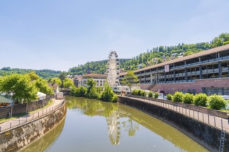 Urban surroundings with a Ferris wheel on the riverbank, wooded hills and clear summer air, Calw,