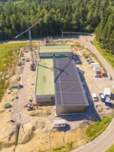 Bird's eye view of a construction site with solar panels and surrounded by forest, visible with