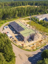 Building complex under construction near the forest, with solar panels and a crane visible, new