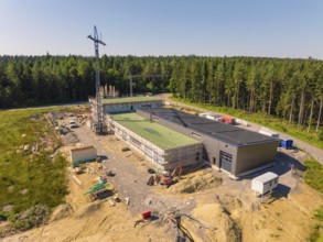Outdoor construction site with solar roof and crane, surrounded by forest in sunny weather, new
