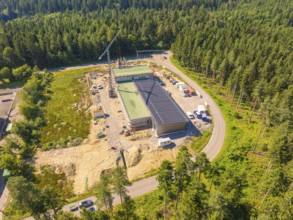 Solar roof building on a construction site surrounded by trees, crane and vehicles visible, aerial