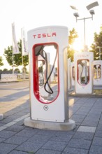 Tesla charging station in urban environment at sunset with light effects, Tesla Supercharger