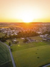 Aerial view of a village at sunset, surrounded by fields and trees, warm and quiet atmosphere,