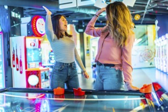 Two women giving high five while playing air hockey, enjoying their time together in entertainment