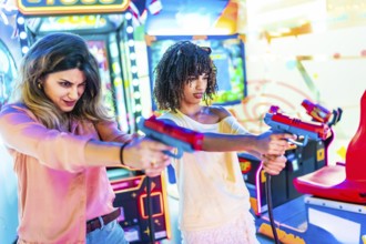 Two young women focusing intently while enjoying a thrilling shooting game in a vibrant amusement