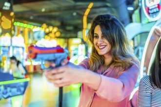 Cheerful young woman holding a toy gun, playing at an arcade game machine, enjoying her free time