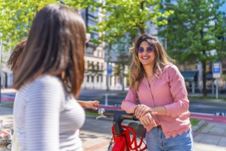 Group of friends talking and smiling next to a red electric scooter in a sunny summer day in the