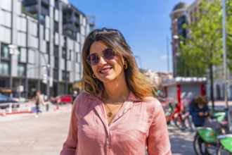 Portrait of a beautiful brunette woman smiling wearing sunglasses in a city on a sunny summer day