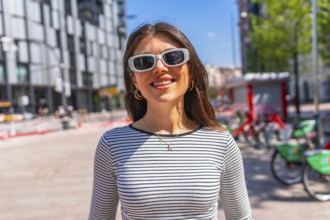 Portrait of a happy young woman wearing sunglasses and a striped shirt in a city center during a