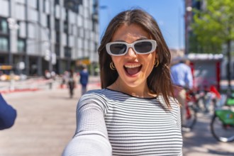 Happy woman wearing trendy sunglasses, joyfully taking a selfie in the bustling city center on a
