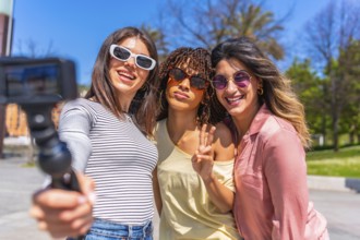 Three joyful women enjoying a sunny day, taking a selfie with an action camera while bonding during
