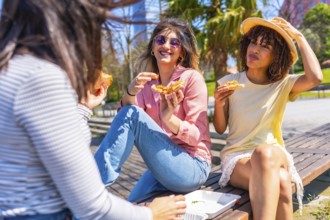 Young multi ethnic women having fun eating pizza slices in a park during a beautiful summer day