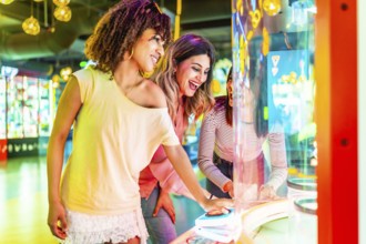 Three cheerful female friends enjoying their time together playing an arcade game in an amusement