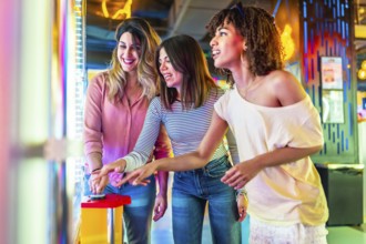 Three female friends enjoying a vibrant summer night out in the city, laughing and playing arcade