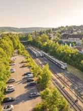 A train runs through a green landscape with trees and a car park, summer atmosphere, Weil der Stadt