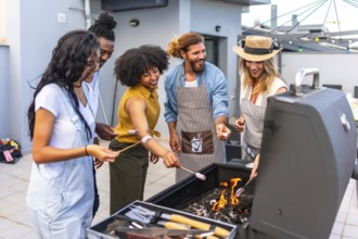Happy friends enjoying a rooftop party, roasting marshmallows over a barbecue grill while sharing