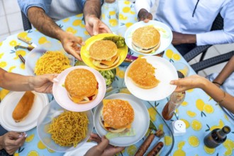 Hands holding plates with hamburgers and fries during a barbecue with friends, sharing food on a
