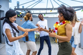 Cheerful young people enjoying drinks and dancing joyfully at a vibrant rooftop party, celebrating