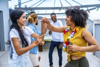Cheerful young friends are dancing and having fun at a rooftop party, enjoying drinks and each