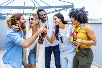 Cheerful multi ethnic friends enjoying drinks at a rooftop party, celebrating their friendship with